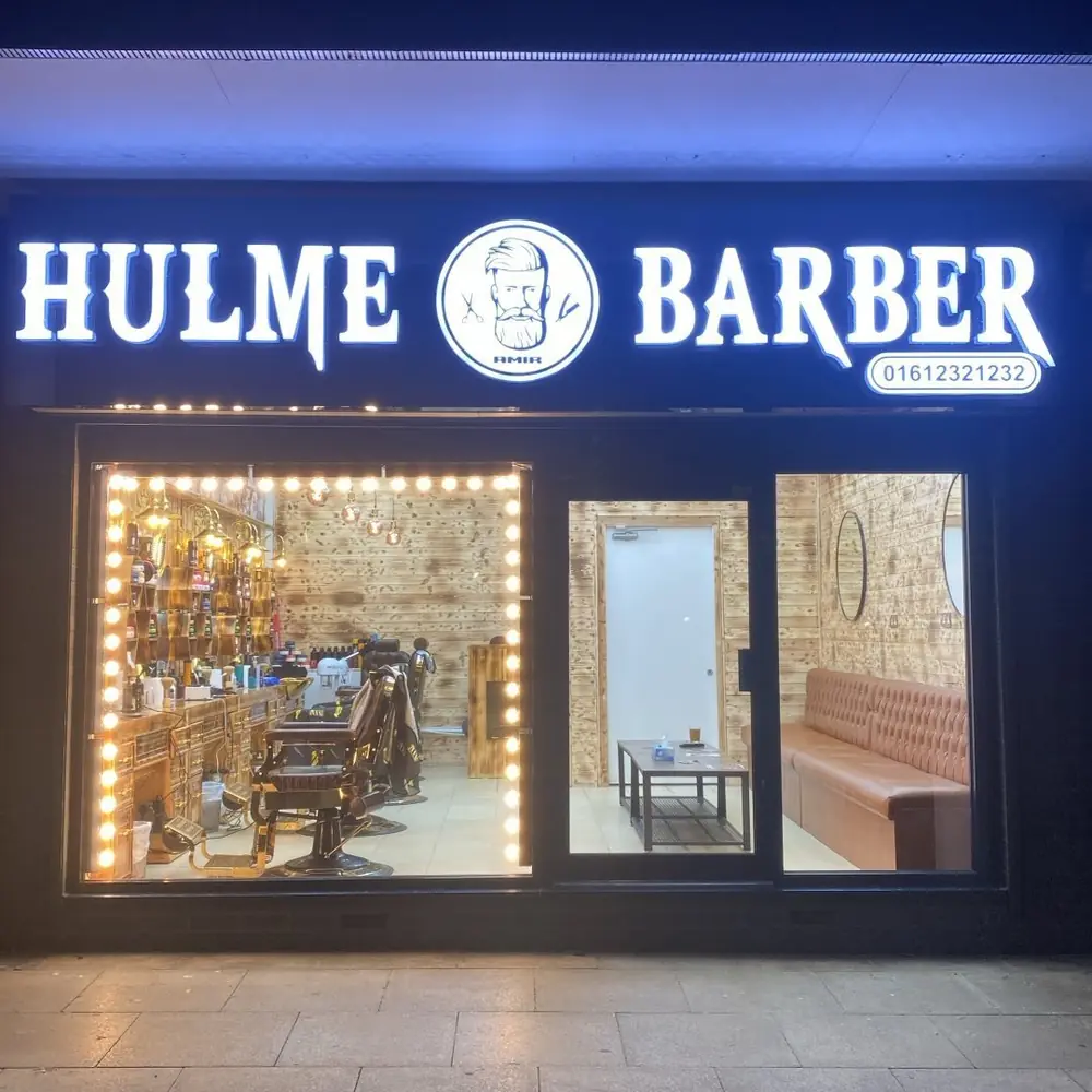 The Hulme Barbers shopfront lit up at night
